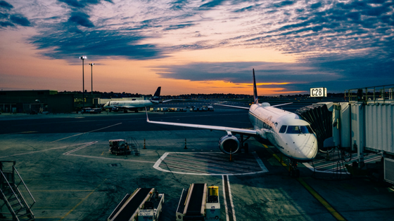 A picture of an airplane at a terminal at an airport with a pretty multicolored dusk sky