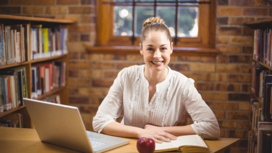 teacher sitting with a computer in a library setting 